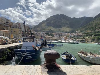 Sailboats moored on harbor by city against sky