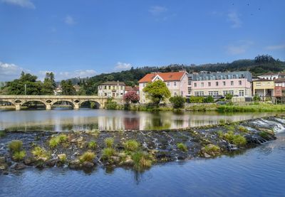 Arch bridge over river by buildings against sky