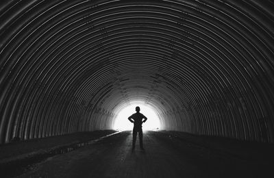 Full length of silhouette boy with hands on hip standing in tunnel