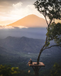 Woman sitting on mountain against sky