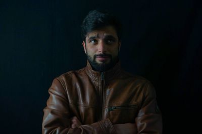 Portrait of young man standing against black background