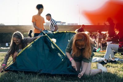 Friends making tent on lawn in music festival during summer