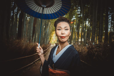 Portrait of woman with umbrella standing in forest