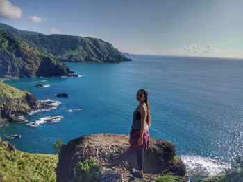 Side view of young woman standing on rock against sea