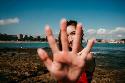 Charming female standing on seashore on sunny day and reaching crossed hands towards camera