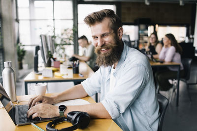 Portrait of smiling male computer programmer typing on laptop while working in office