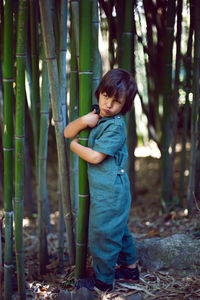 Boy child in a green jumpsuit walks among tall bamboos in the summer afternoon