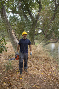 Full length of man holding chain saw standing in forest