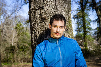 Beautiful man with blue eyes. the man is training in the woods and is leaning against an oak tree.