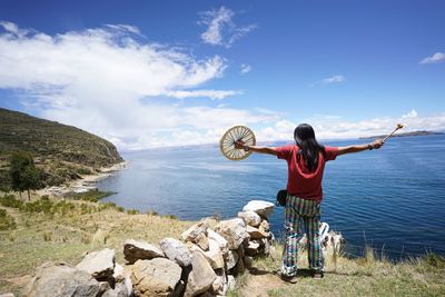 Rear view of man standing on grass at shore against sky