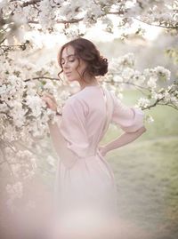 Portrait of woman with pink flower standing by tree