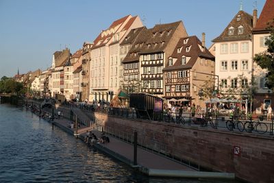 Buildings by river in city against clear sky