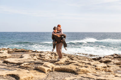 Happy couple on seaside. man carries his girlfriend along rocky beach of saint julian area of malta.