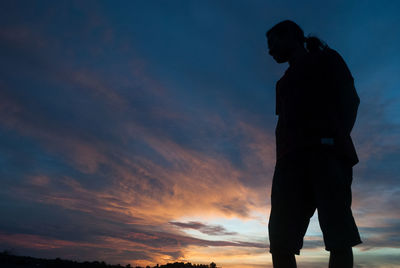 Low angle view of man standing against cloudy sky during sunset