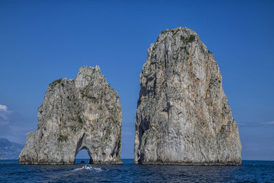 Rock formation in sea against clear blue sky