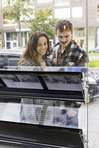 Smiling young couple looking at placard on glass window of real estate office