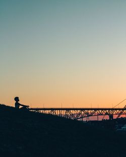 Silhouette man standing by bridge against sky during sunset