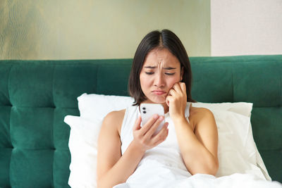 Young woman using mobile phone while lying on bed at home