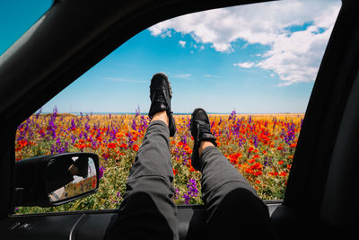 Low section of woman traveling in car against colorful meadow and sky in summer