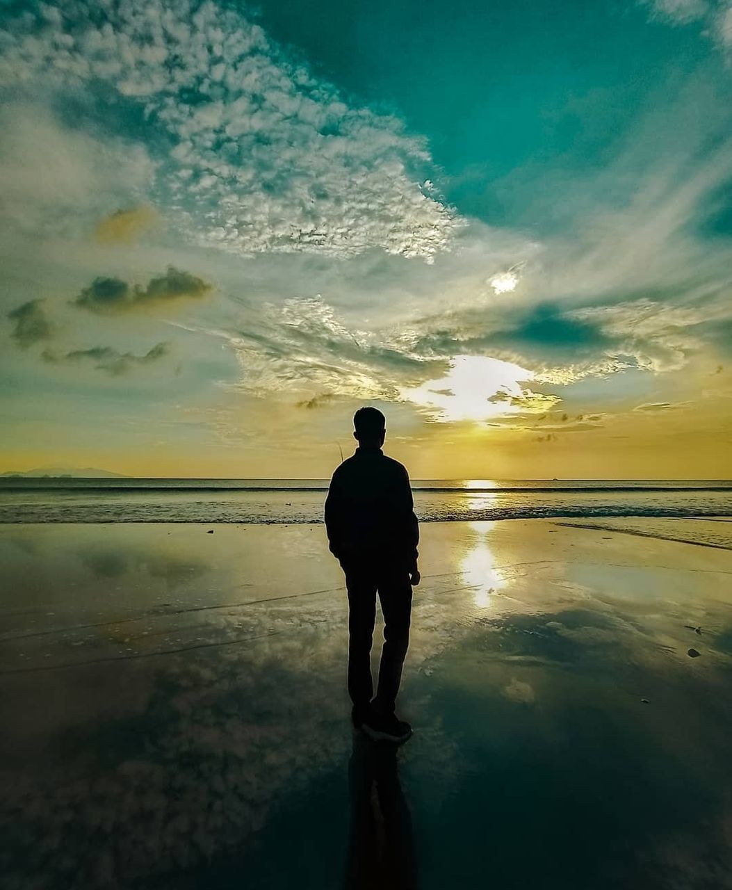 water, sky, horizon, sea, ocean, reflection, one person, cloud, beach, sunset, sunlight, silhouette, nature, beauty in nature, land, men, standing, dusk, full length, rear view, scenics - nature, evening, adult, wave, coast, tranquility, shore, person, sun, outdoors, horizon over water, tranquil scene, contemplation, vacation, solitude, leisure activity, trip, idyllic, holiday, lifestyles, back lit, environment