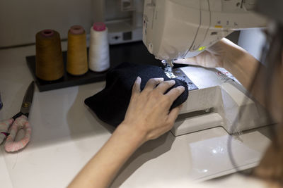 Woman is sewing black beanie hat on a sewing machine, using a sewing machine on the sewing table