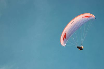 Low angle view of person paragliding against blue sky