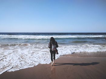 Rear view of woman walking at beach against clear sky