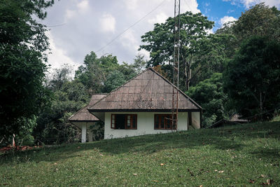 House on field by trees against sky