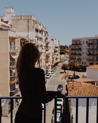 Rear view of silhouette woman standing in balcony against buildings in city