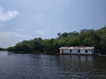 House and trees by lake against sky