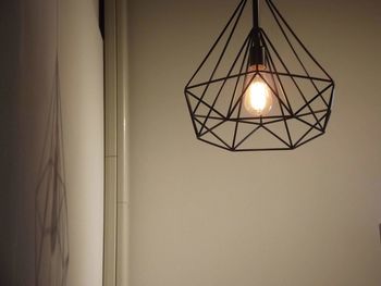 Low angle view of illuminated pendant light hanging against wall