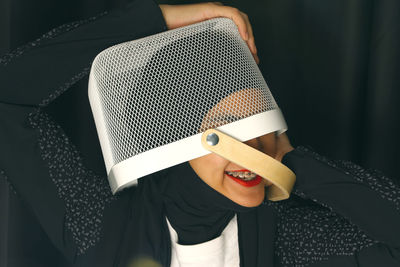Young woman in hijab with basket on head against black background