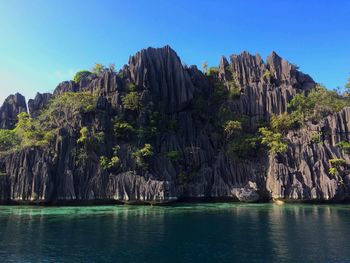 Scenic view of rocks by sea against clear sky