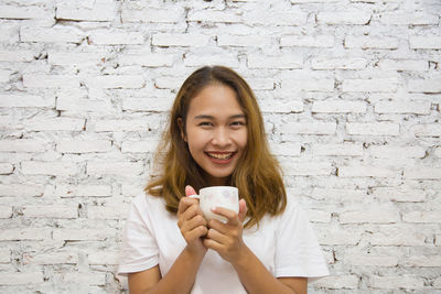 Portrait of a young woman with coffee cup against wall