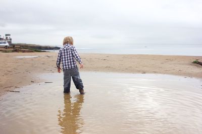 Rear view of boy standing on beach against sky