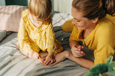 A little daughter playing with mother and paints her nails with polish.