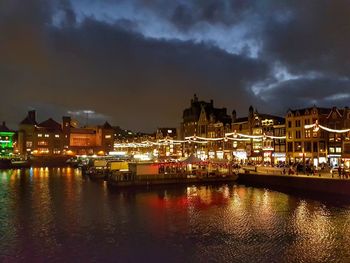 Illuminated cityscape by river against sky at night