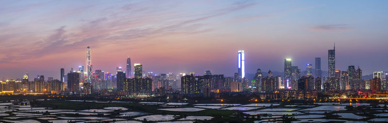 Illuminated buildings in city against sky during sunset