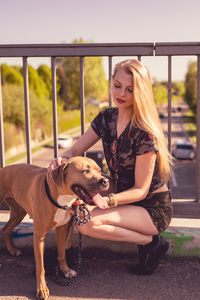 Smiling young woman sitting by dog on footbridge