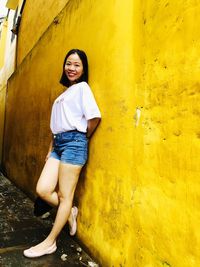 Portrait of smiling young woman standing against yellow wall