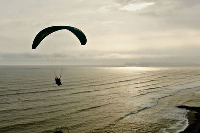 Person paragliding over sea against sky