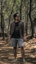 Young man looking away while standing in forest