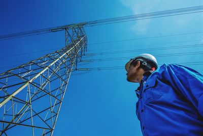 Low angle view of engineer standing by electricity pylon against clear blue sky