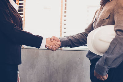 Midsection of business colleagues shaking hands against window