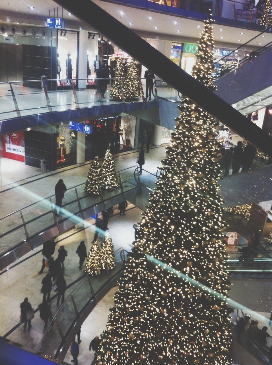 indoors, ceiling, built structure, architecture, illuminated, large group of people, shopping mall, modern, glass - material, hanging, high angle view, incidental people, lighting equipment, decoration, reflection, person, transparent, abundance, city