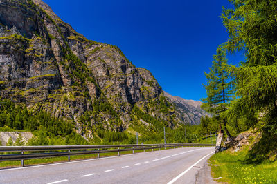 Road amidst trees and mountains against clear blue sky