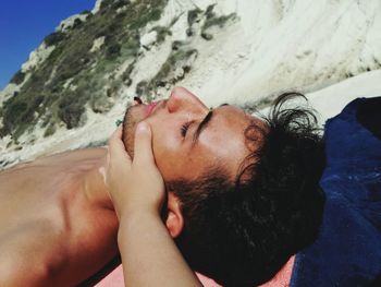 Hand touching face of man while relaxing at shore of beach