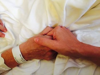 Cropped image of man holding woman hand on bed at home