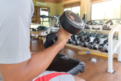 Midsection of man lifting dumbbell in gym