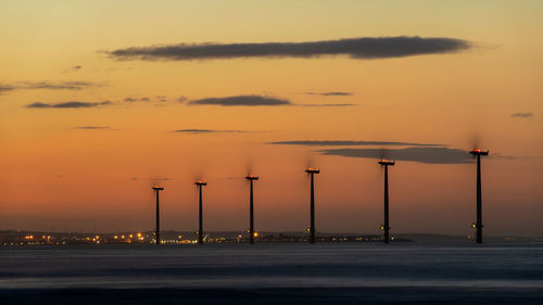 Windmills in sea against sky during sunset